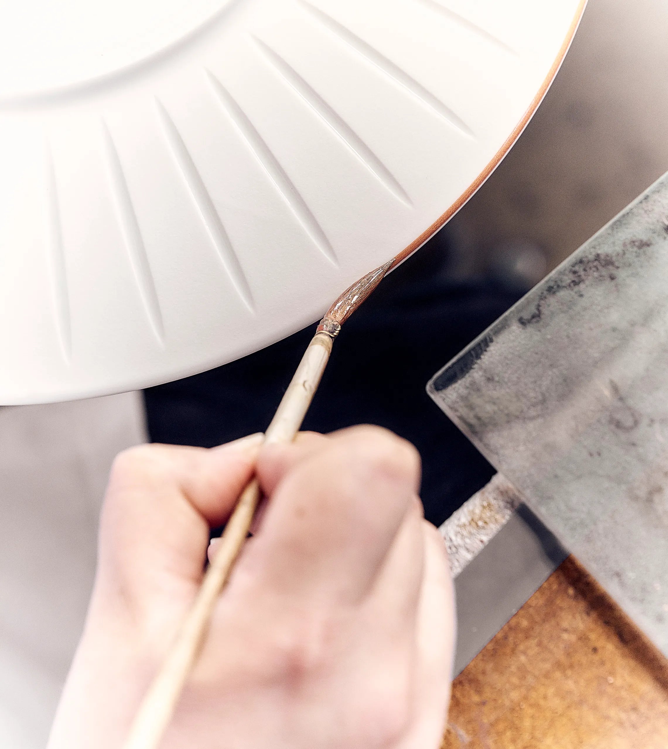  French artisan hand-painting the edge of a porcelain plate, highlighting french porcelain plates craftsmanship, porcelain manufactory tradition, quality dinnerware, unique patterns and alabaster white style from century French manufacturers.